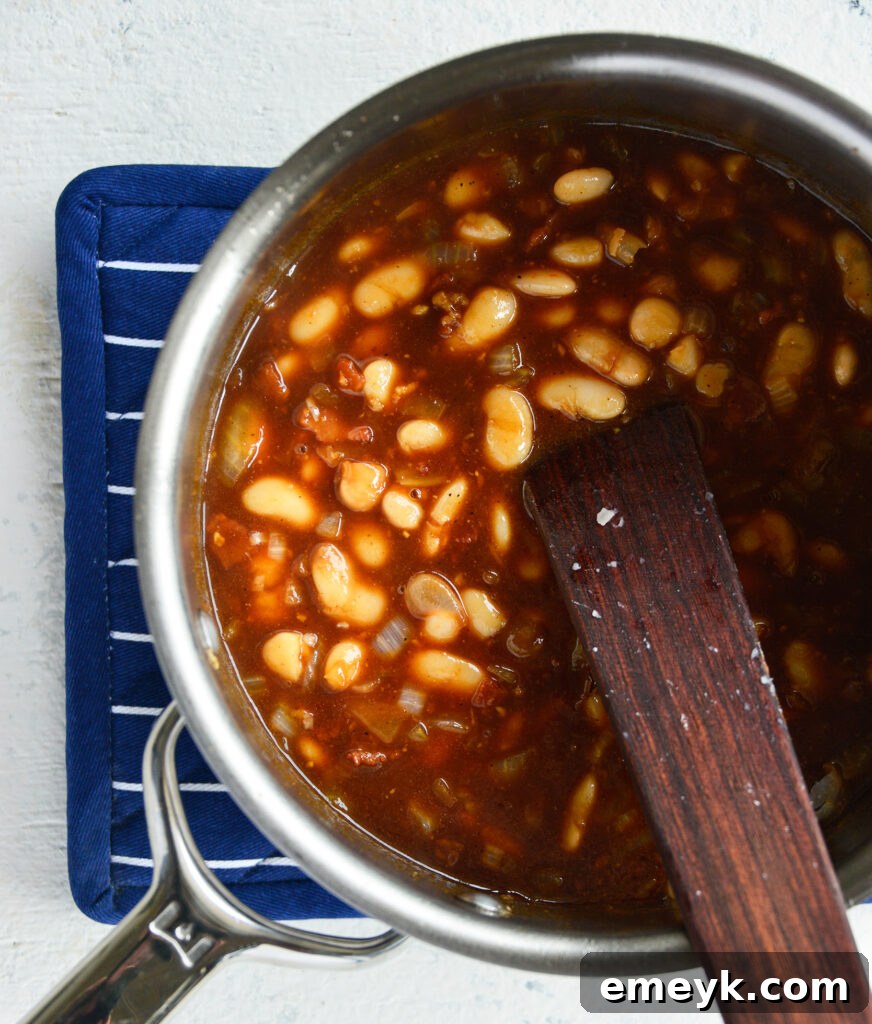 Easy Bacon Baked Beans with a wooden spoon in a pot.