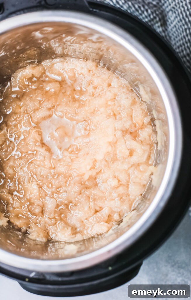 Cooked apples being mashed inside the Instant Pot to create homemade applesauce.