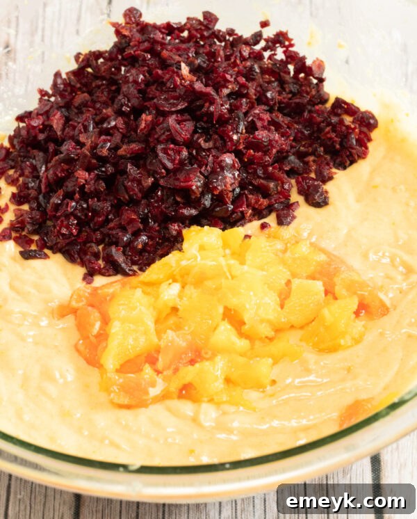 Dried cranberries and orange segments being folded into bread batter.