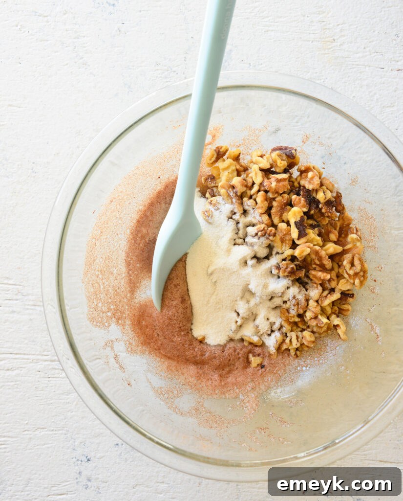 Raw walnuts being stirred into the foamy egg white and sugar mixture in a mixing bowl, ensuring an even coating.