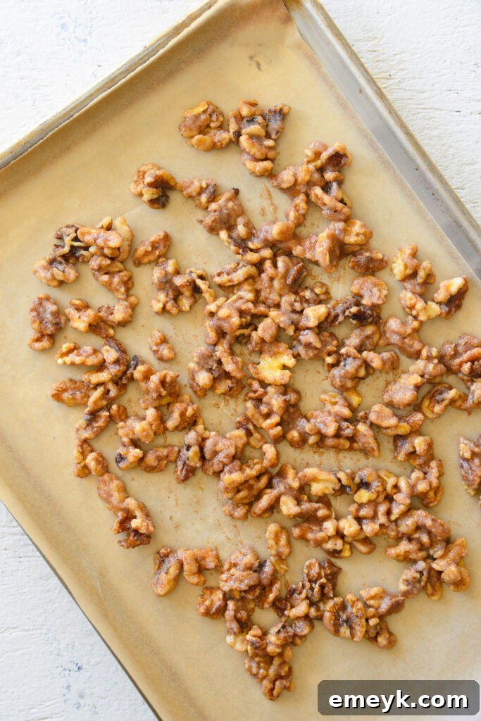 Coated walnuts spread evenly in a single layer on a parchment-lined baking sheet, ready for the oven.