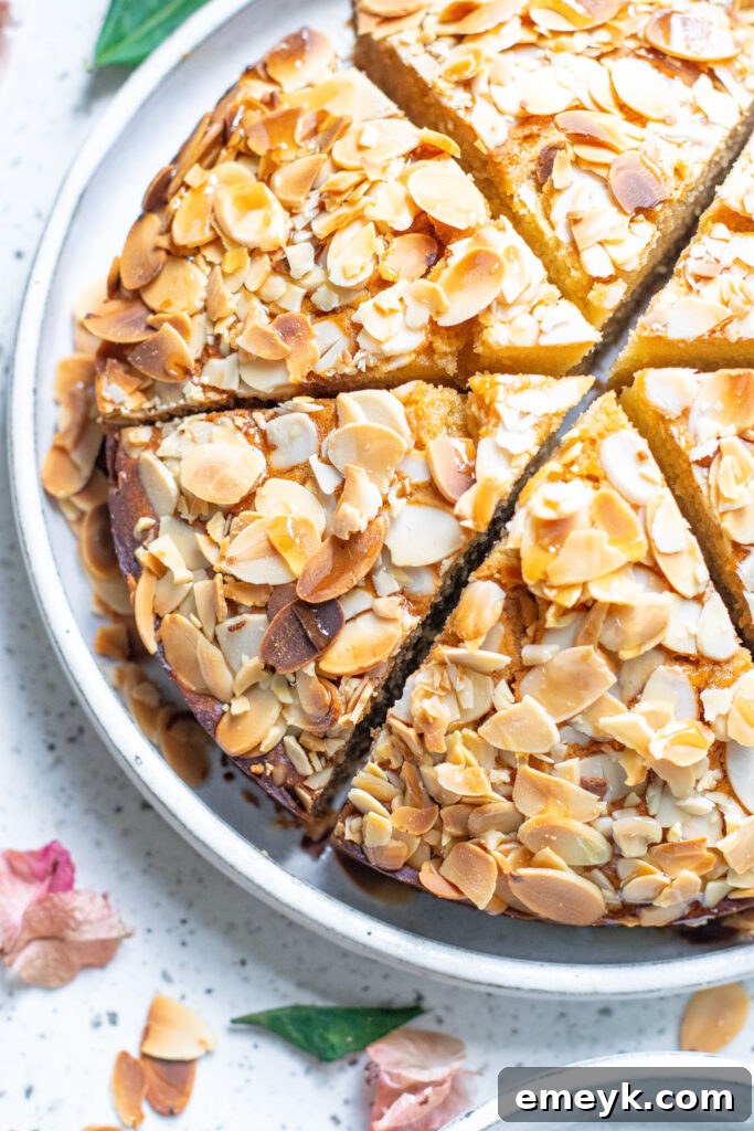 A beautifully baked Honey Almond Cake slice on a pristine white plate, garnished with fresh berries and a light dusting of powdered sugar, highlighting its moist texture and golden-brown crust.