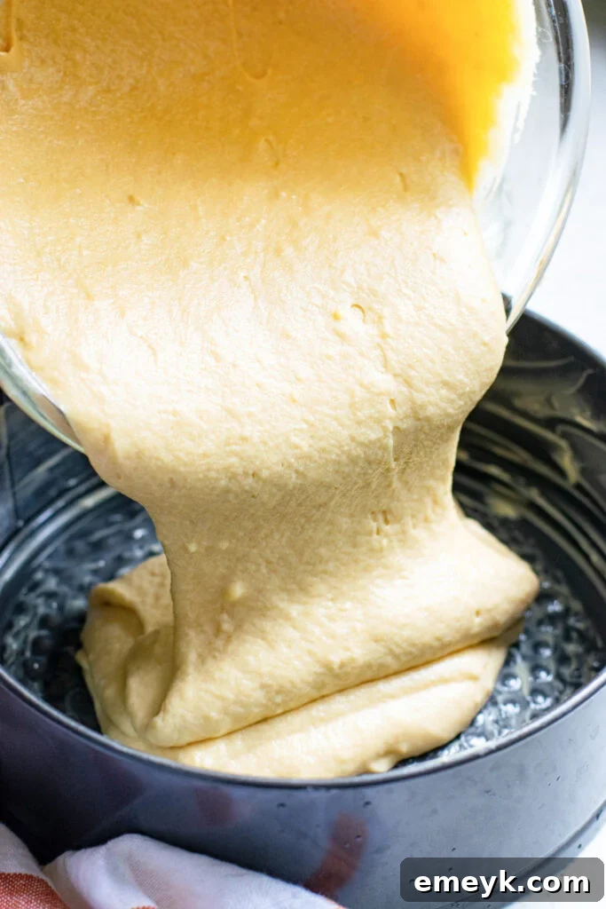The smooth Honey Almond Cake batter being carefully poured from a mixing bowl into a prepared 9-inch circular baking pan, ready for the almonds and baking process.