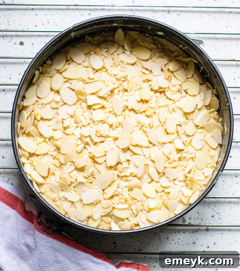 A freshly baked Honey Almond Cake, golden brown with toasted slivered almonds, still in its 9-inch baking pan, cooling on a wire rack, steam gently rising.