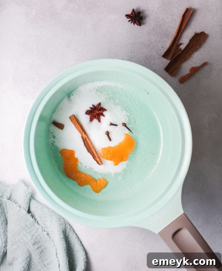 A small pot contains the rich, spiced simple syrup for the Cranberry Wine Spritzer, with orange peels and whole spices visible, infusing flavor.