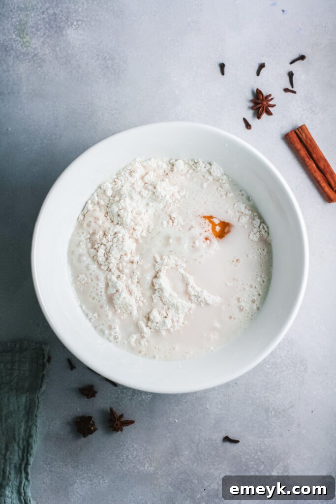 Eggnog pancake batter being mixed in a bowl, with a small grater and whole nutmeg on the side