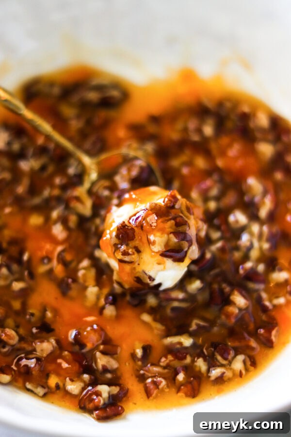 A Honey Goat Cheese Ball being coated with the pecan and apricot mixture using a spoon.