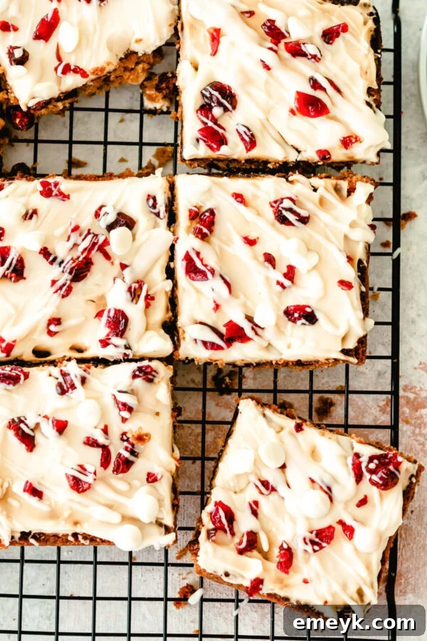 Cranberry Bliss Bars on wire rack, glistening with cream cheese frosting and white chocolate drizzle, ready for holiday enjoyment.