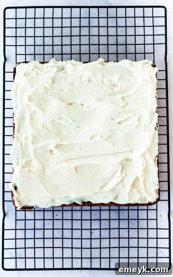 Cranberry Bliss Bars generously topped with creamy white cream cheese frosting, ready for the final touches of cranberries and white chocolate drizzle.