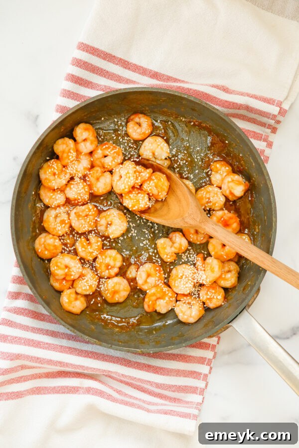 Sticky Sriracha Honey Garlic Shrimp 7 Cooked shrimp being coated in the sweet and spicy sauce in a skillet.