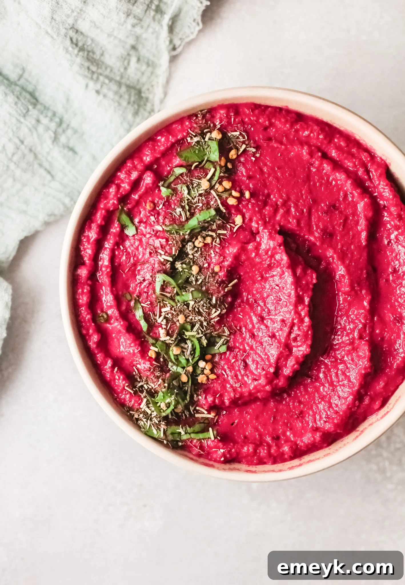 A beautifully presented bowl of Easy Beet Hummus, garnished with fresh herbs and a drizzle of olive oil.