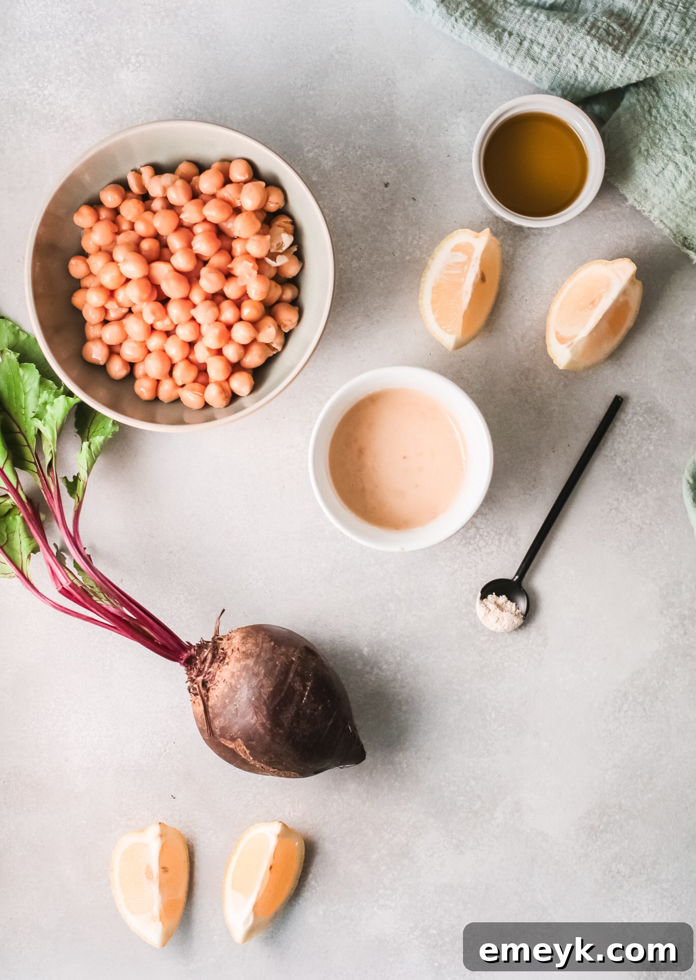 Raw beets, canned chickpeas, tahini, fresh lemons, and garlic cloves laid out as ingredients for Beet Hummus.