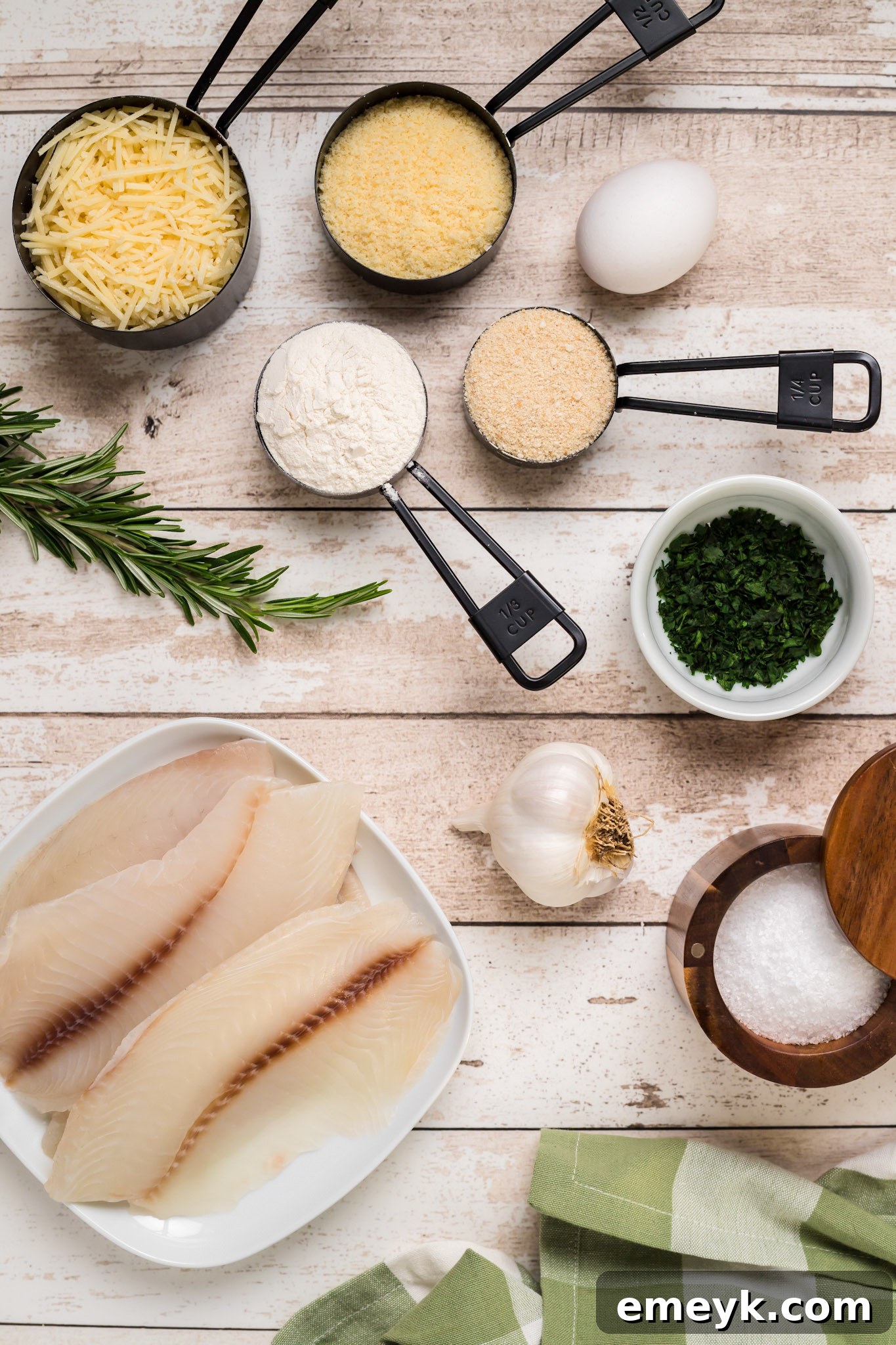 Fresh ingredients laid out for Parmesan Crusted Tilapia: tilapia fillets, Parmesan cheese, flour, breadcrumbs, herbs, garlic, egg, and olive oil.