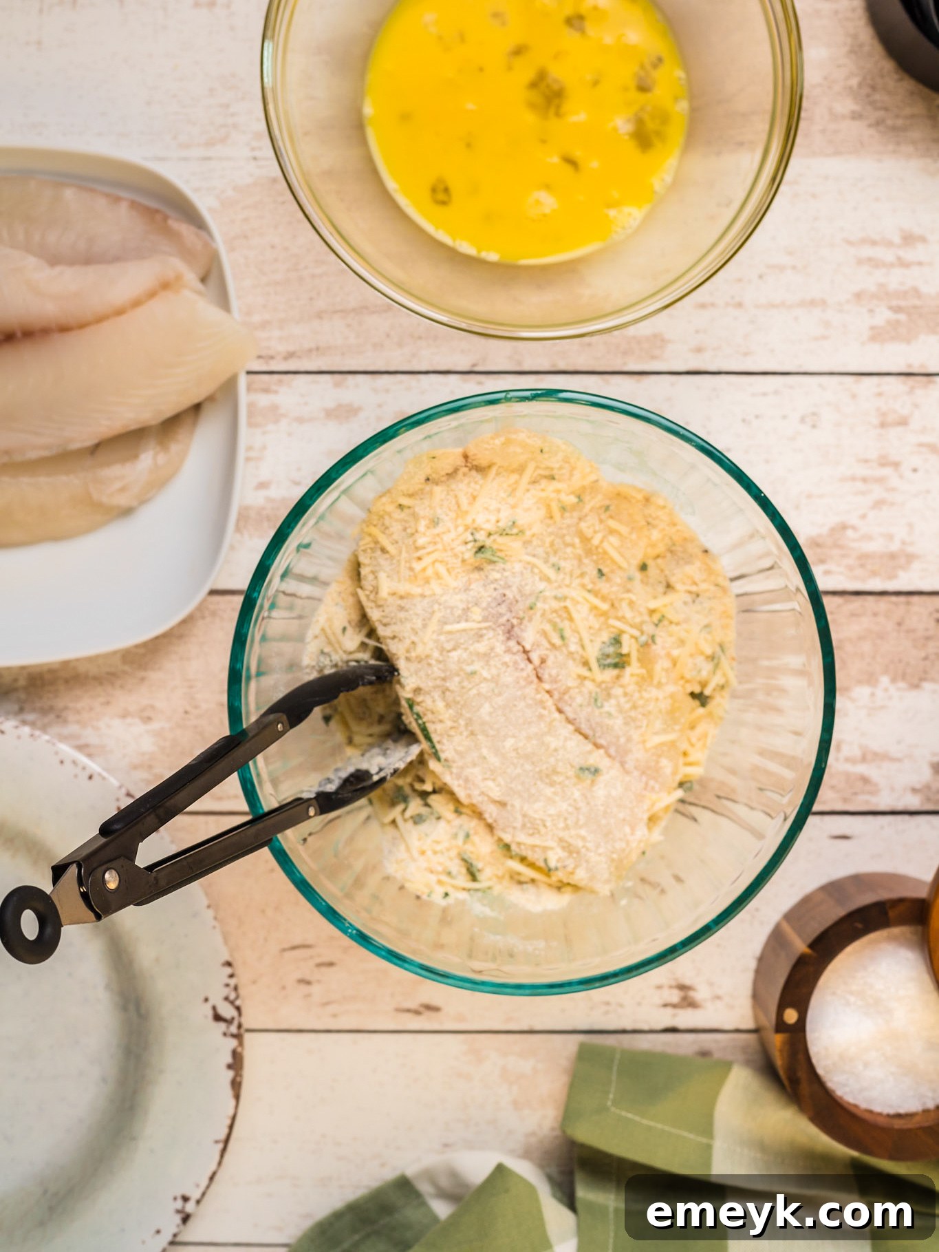 Using tongs to coat a tilapia fillet in the Parmesan breadcrumb mixture.