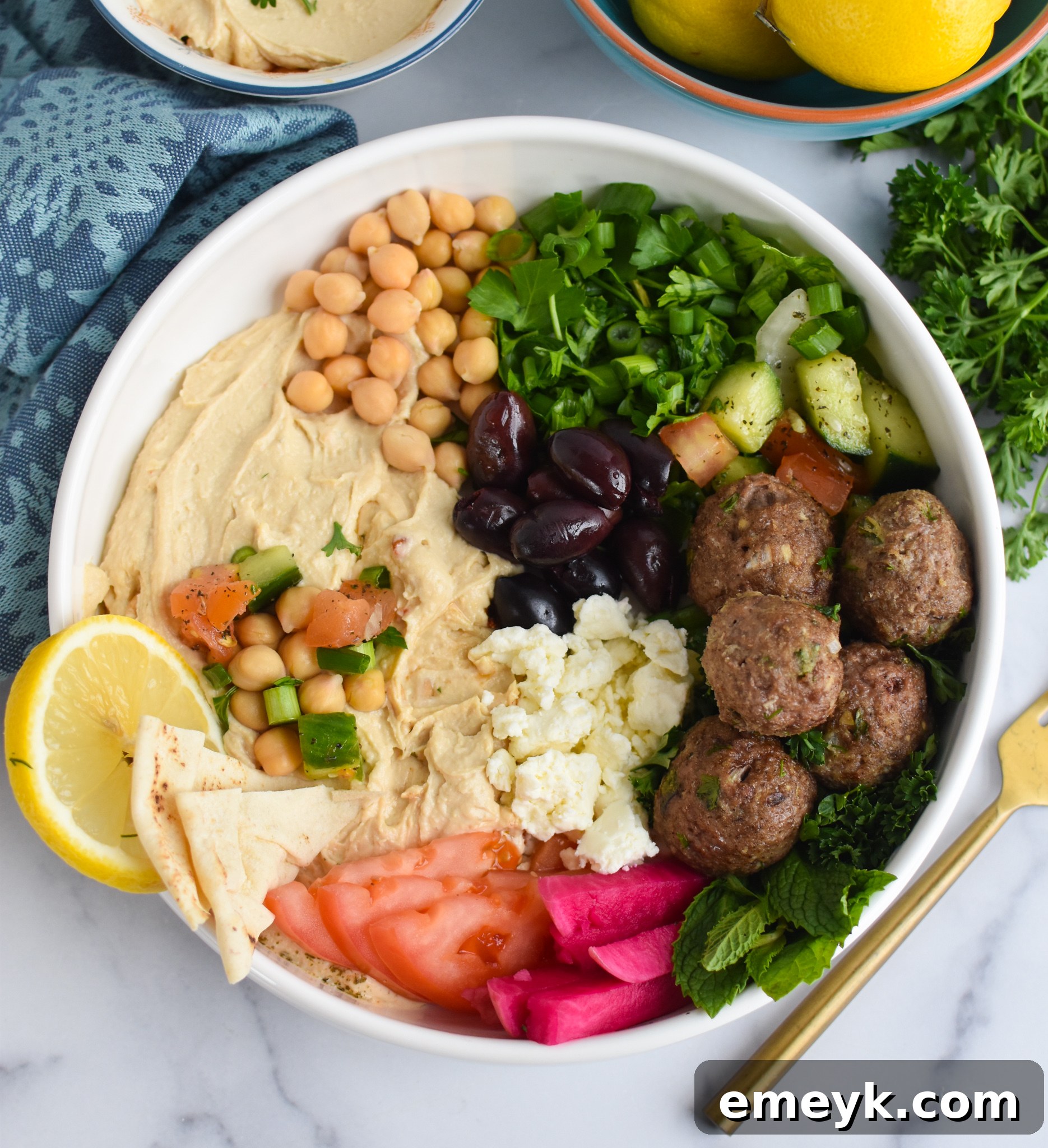 Spiced Lamb Kofta 3 A vibrant bowl of Lamb Kofta served on a bed of creamy hummus, adorned with crumbled feta cheese, fresh diced tomatoes, crisp cucumber slices, and chopped green onions, ready for a delicious meal.