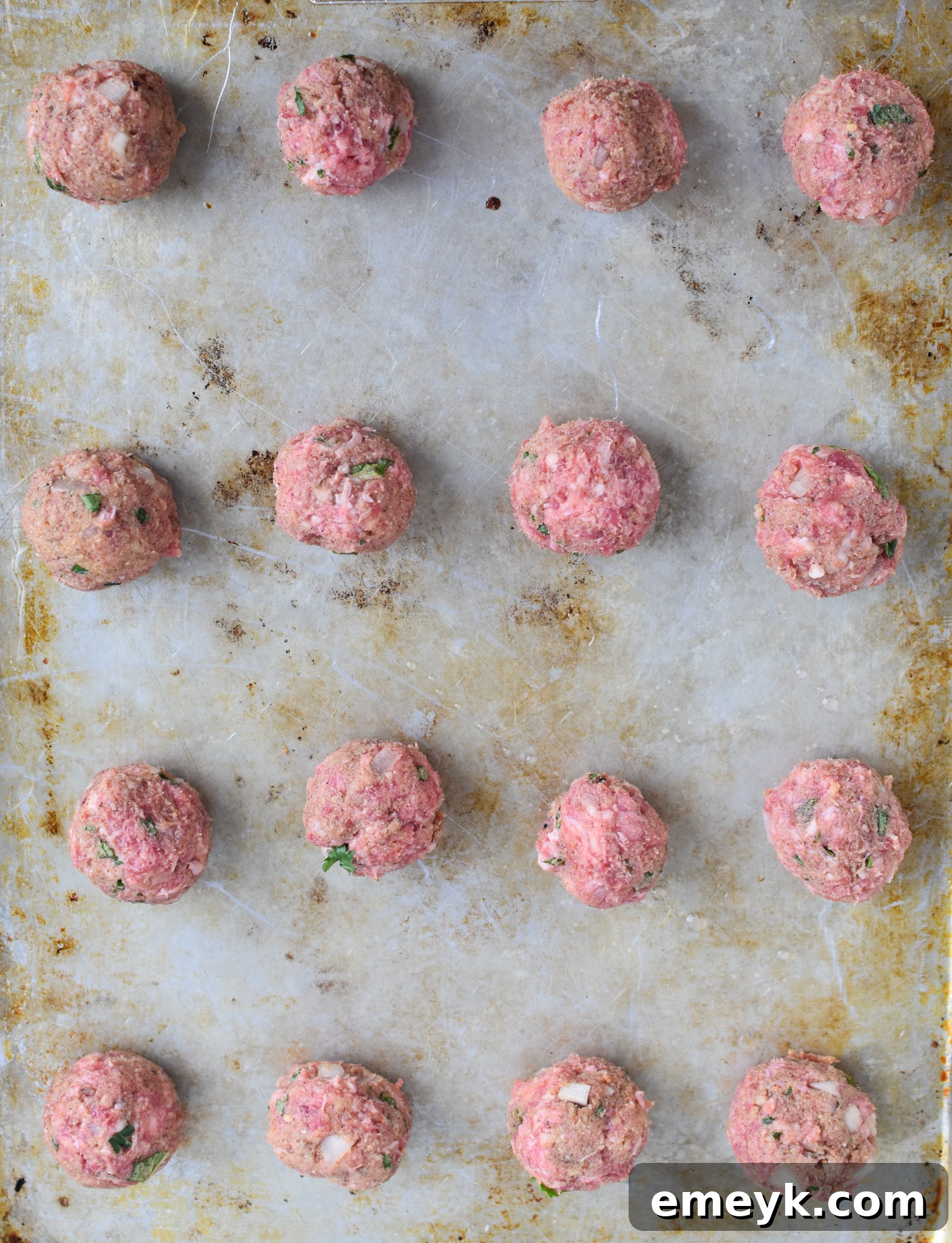 Spiced Lamb Kofta 7 Raw Lamb Kofta meatballs, perfectly shaped and arranged neatly in rows on a baking sheet, showcasing their readiness for baking or grilling.