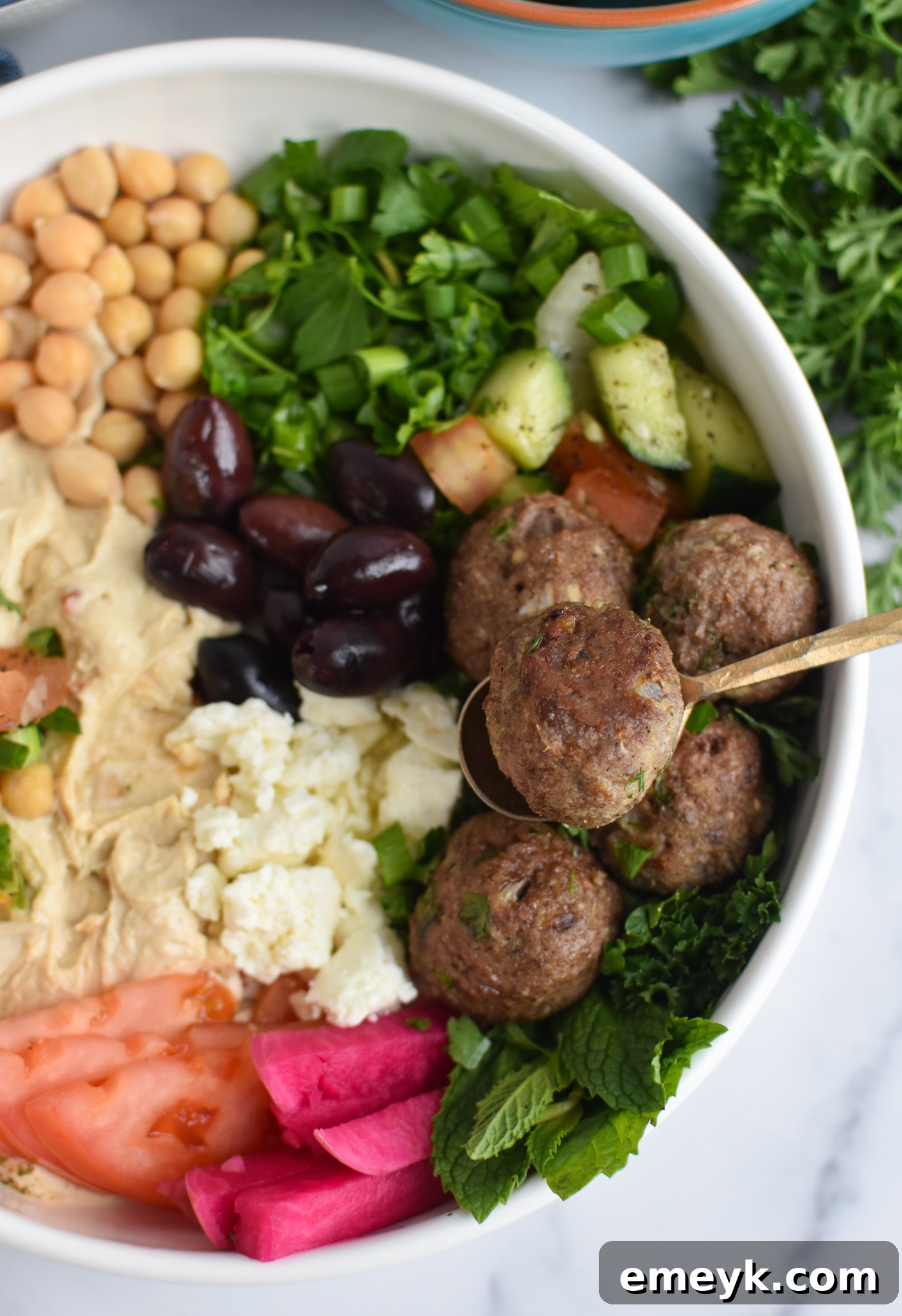 Spiced Lamb Kofta 8 A close-up of a delightful Lamb Kofta hummus bowl, featuring a perfectly cooked kofta meatball nestled in creamy hummus, adorned with fresh herbs and a drizzle of olive oil, accompanied by a fork.