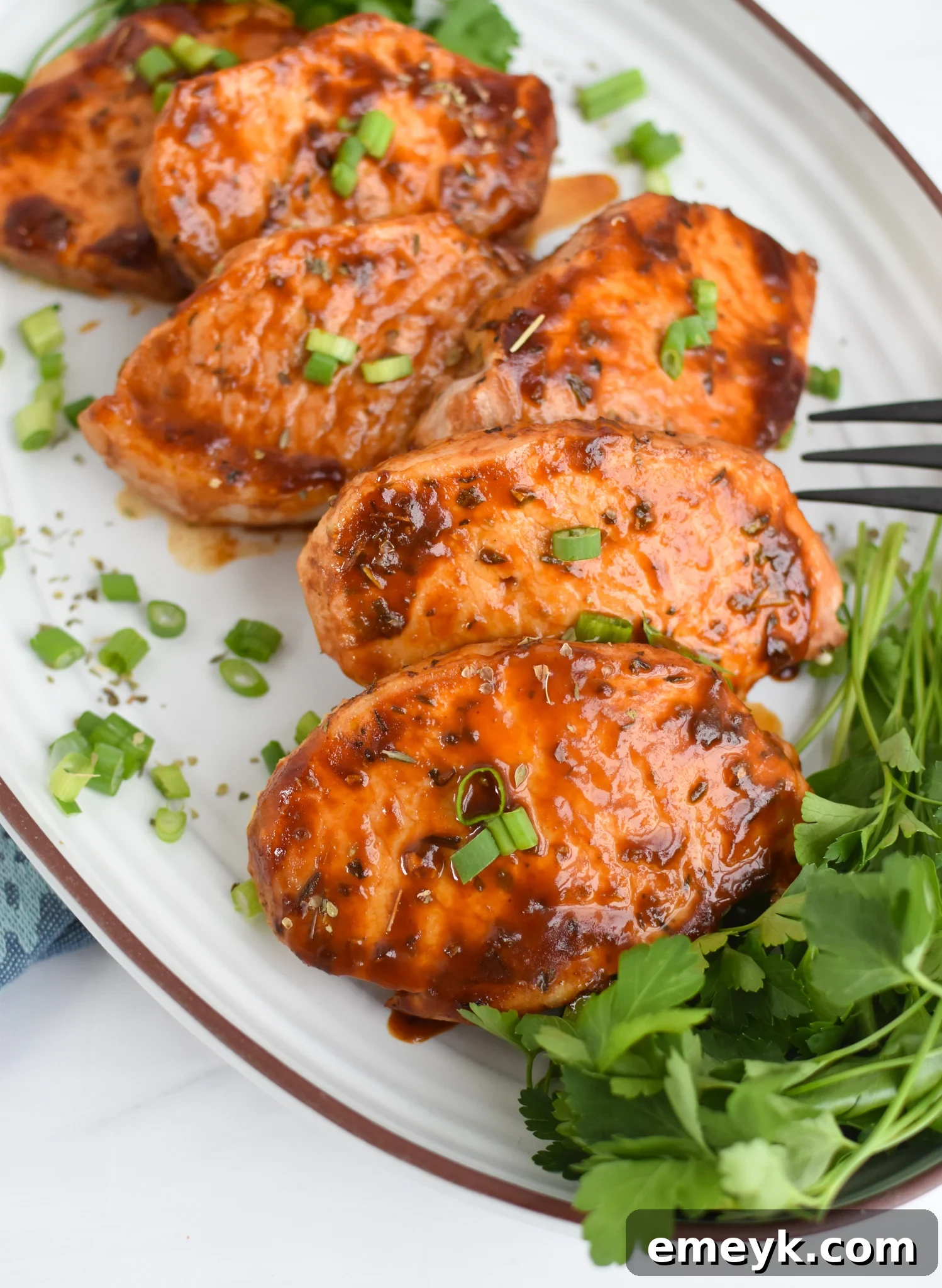 Succulent Baked BBQ Pork Chops 2 BBQ Baked Pork Chops on a white platter, garnished with fresh herbs.