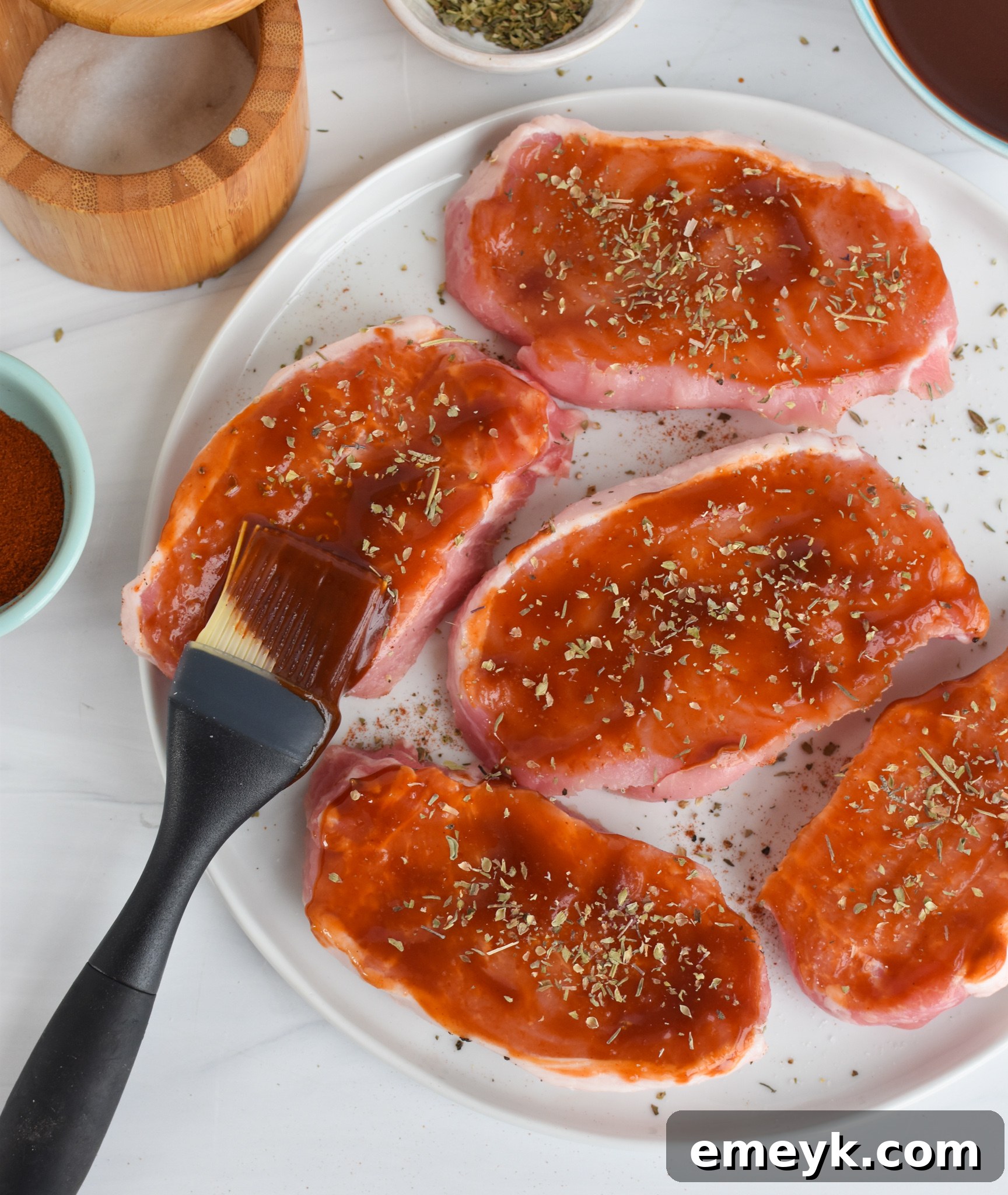 Succulent Baked BBQ Pork Chops 6 BBQ Baked Pork Chops with a basting brush and a bowl of BBQ sauce.