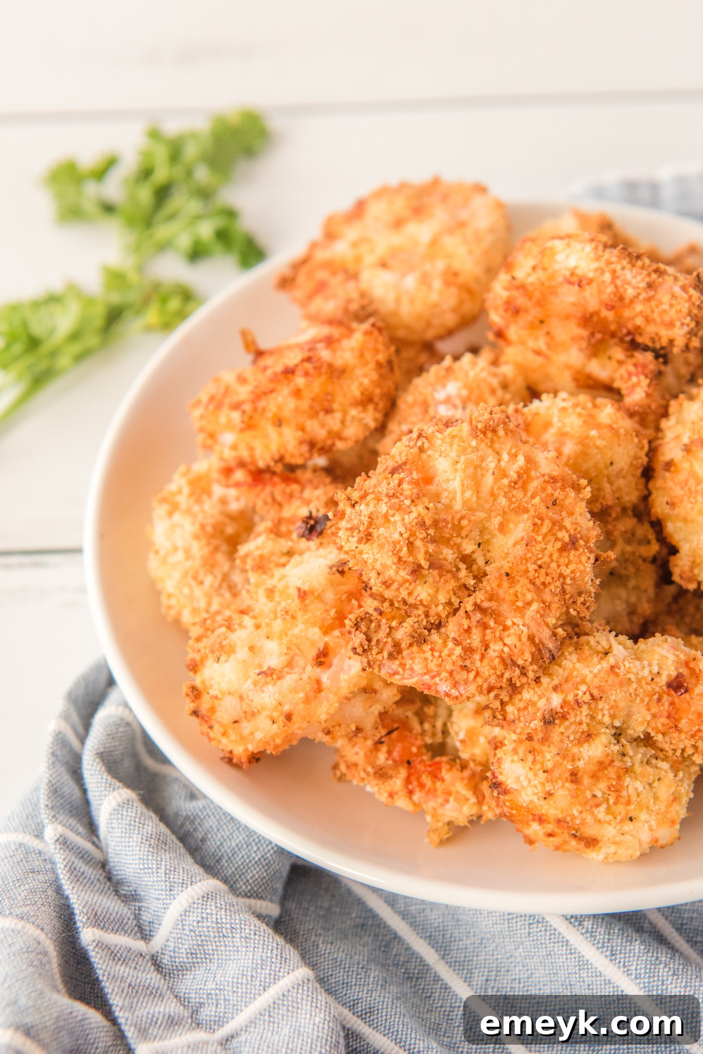Finished Air Fryer Coconut Shrimp arranged neatly on a plate with a garnish of fresh herbs.