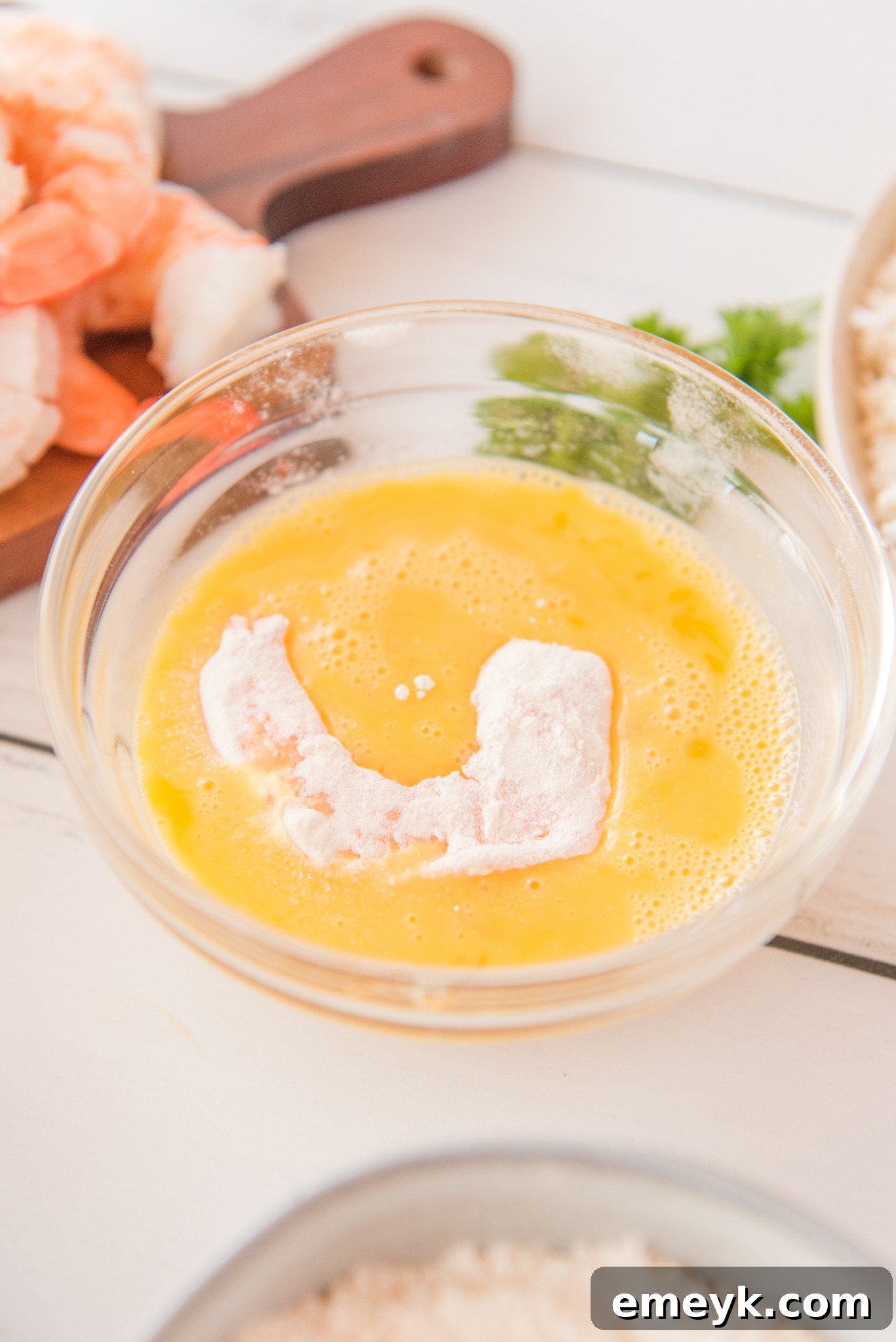 Shrimp submerged in egg wash for air fryer coconut shrimp.