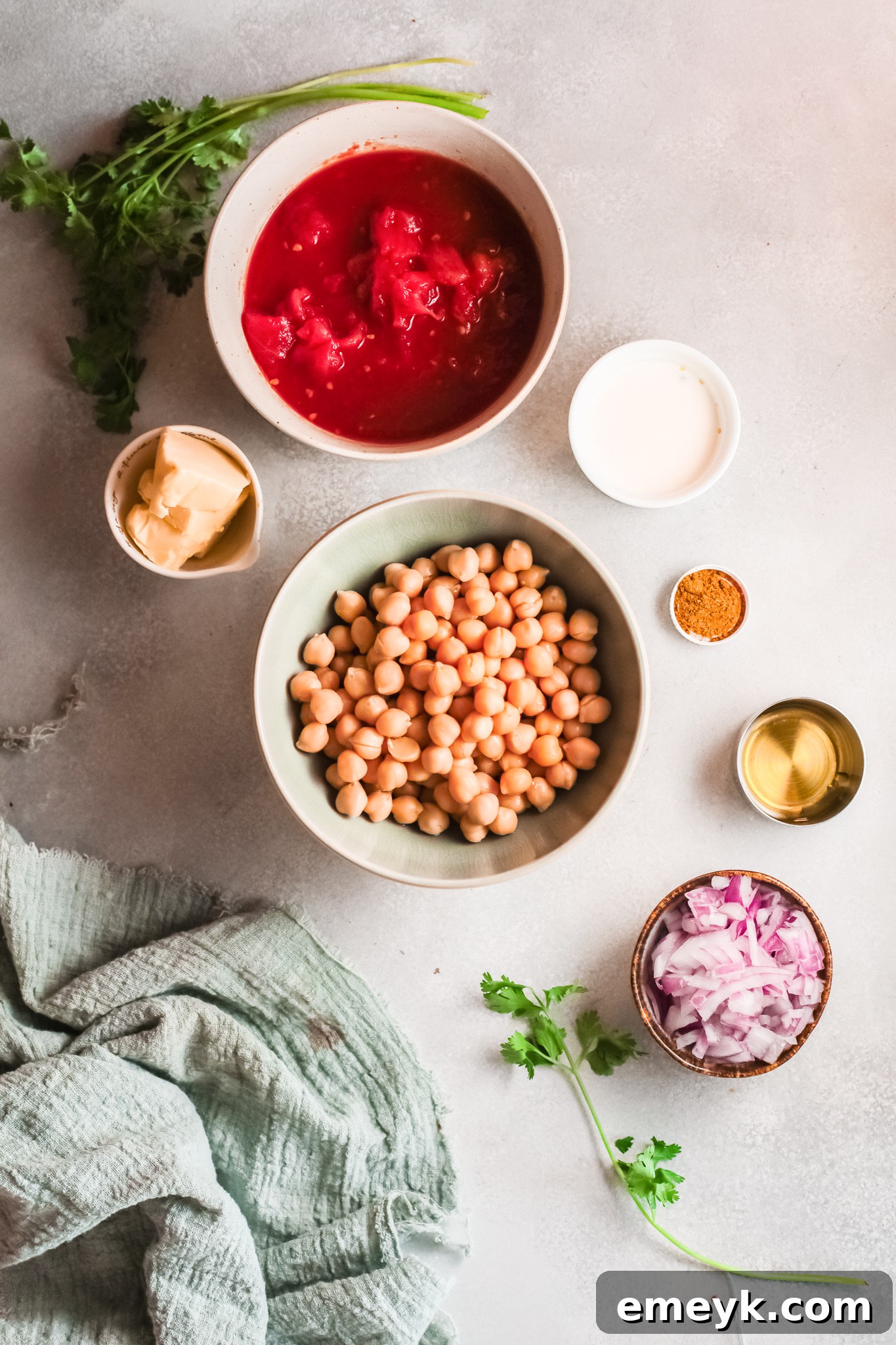 Fresh ingredients laid out for making chickpea curry: canned tomatoes, chickpeas, curry powder, heavy cream, butter, onion, garlic.