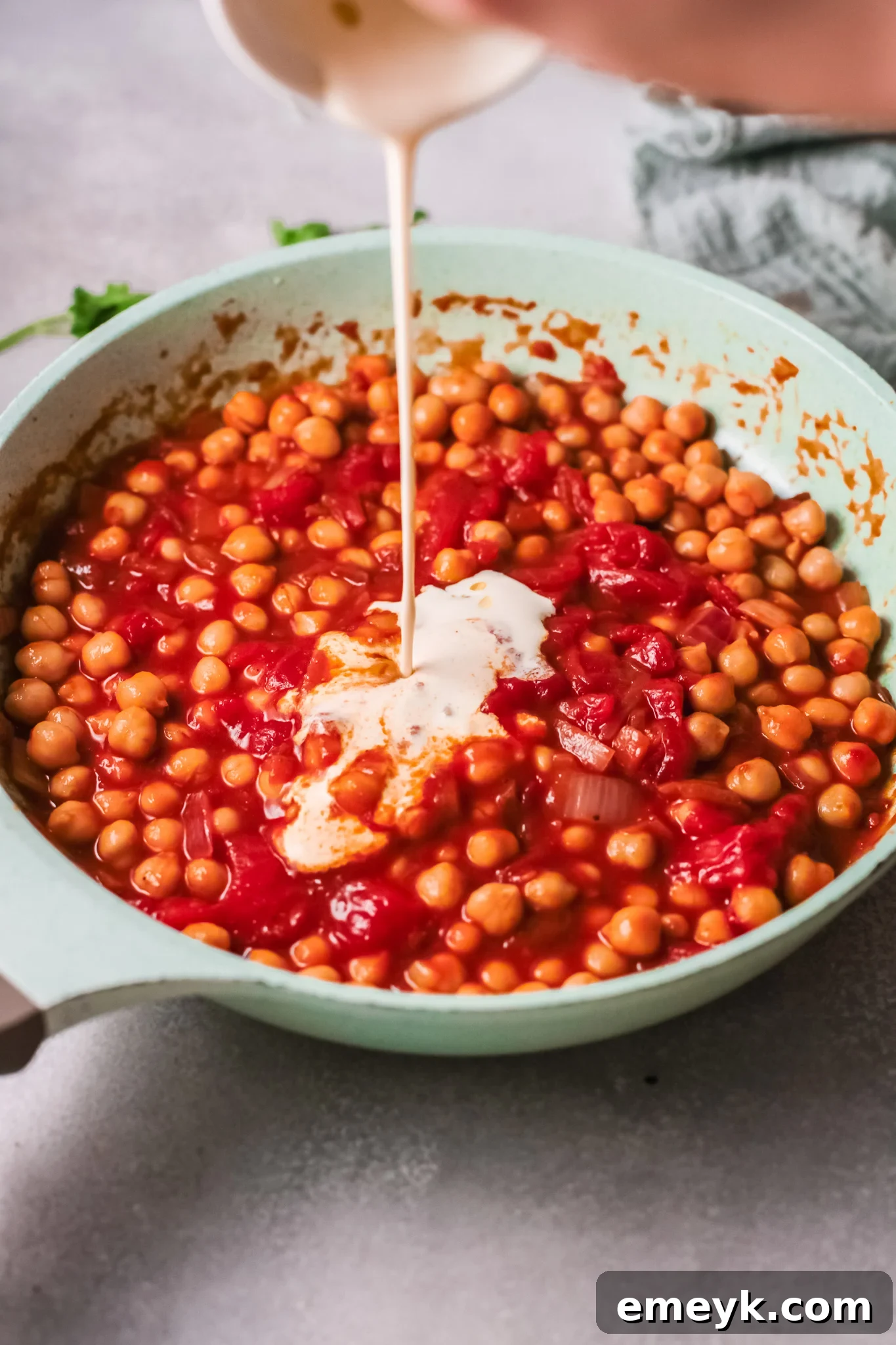 Heavy cream being stirred into the chickpea curry in a pan.