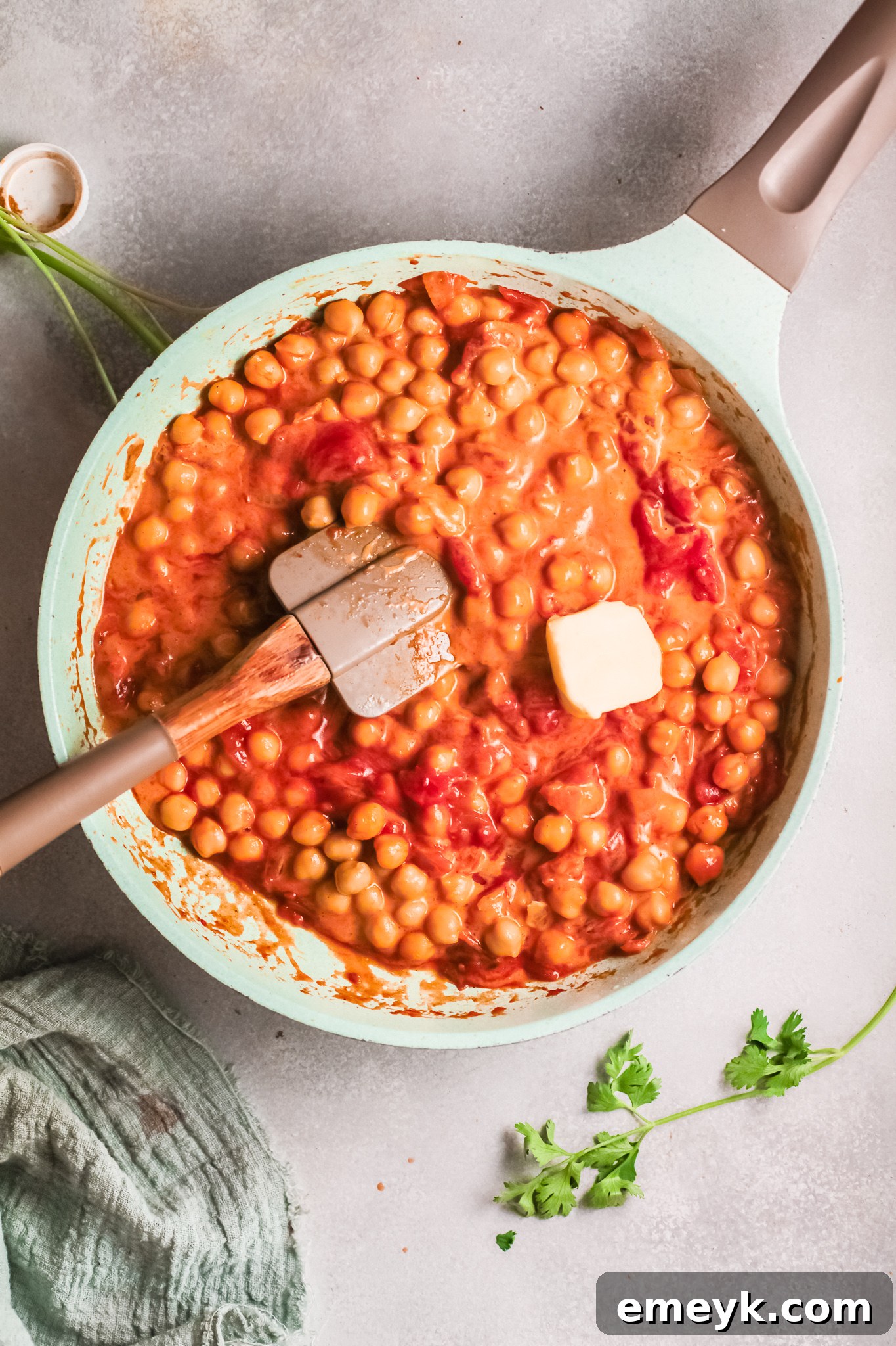 A knob of butter melting into the finished chickpea curry in a pan.