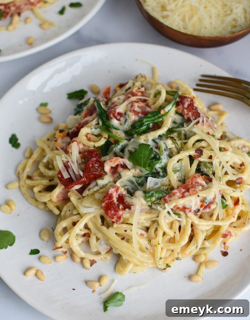 A serving of Creamy Sun-Dried Tomato Pasta on a white plate, garnished with fresh herbs and Parmesan.