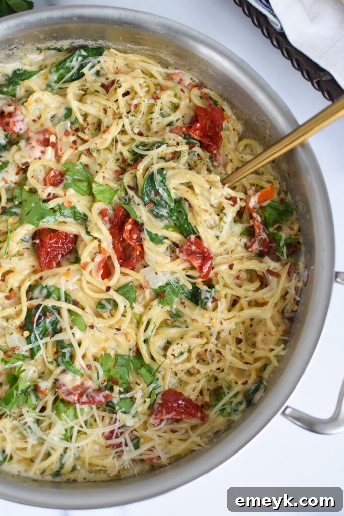 A close-up of Creamy Sun-Dried Tomato Pasta in a pan, with a spoon serving a portion.