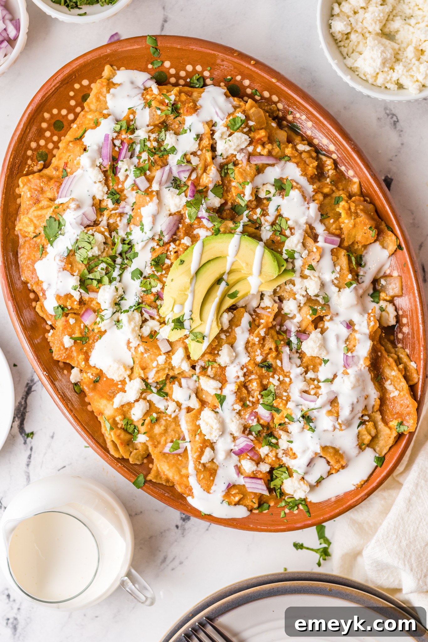 Chilaquiles Rojos Recipe in a large platter topped with avocado slices and Mexican crema.