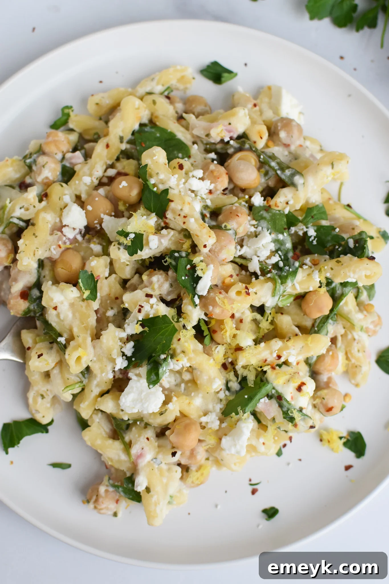 A white plate filled with creamy chickpea pasta with feta, lemon, and fresh arugula on top.