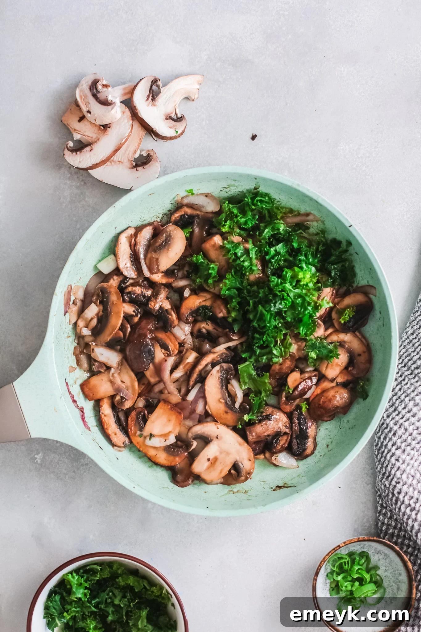 Kale wilting in a skillet with mushrooms, onion, and garlic.