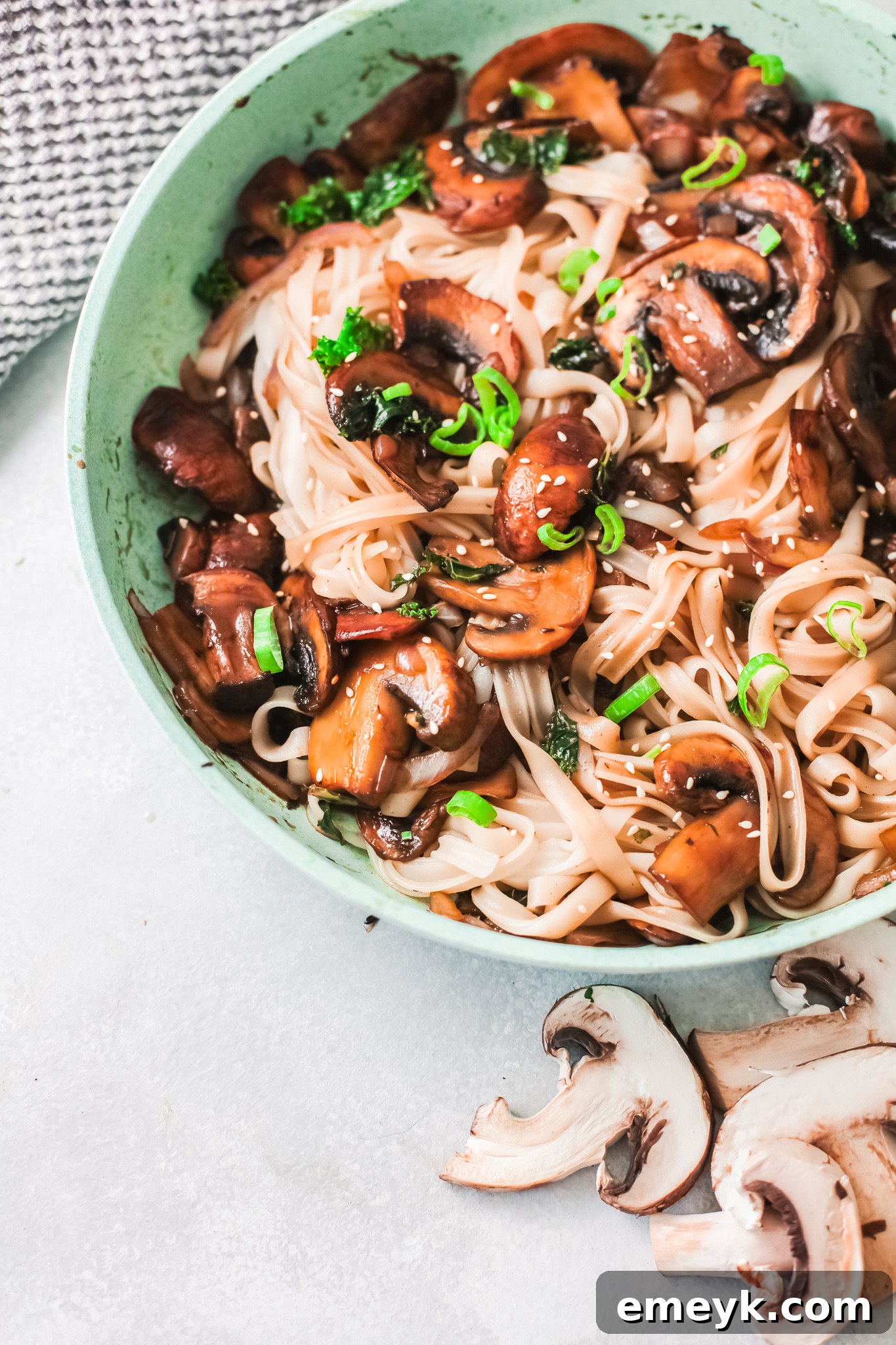 Finished Korean noodles in a skillet, garnished with green onions and sesame seeds.