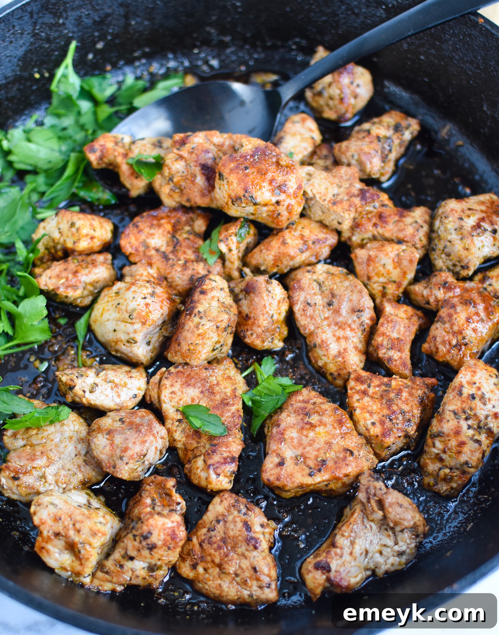 Cast Iron Pork Tenderloin cubes being stirred in a hot skillet with a spoon.