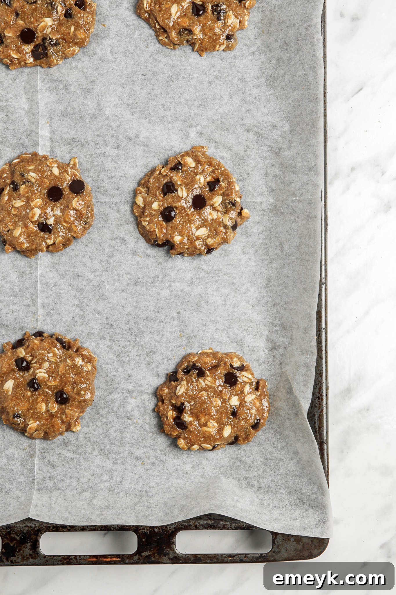 Banana Bliss Oatmeal Cookies 8 Flattened portions of Homemade Banana Oatmeal Cookies dough on a parchment-lined baking sheet, ready for the oven.