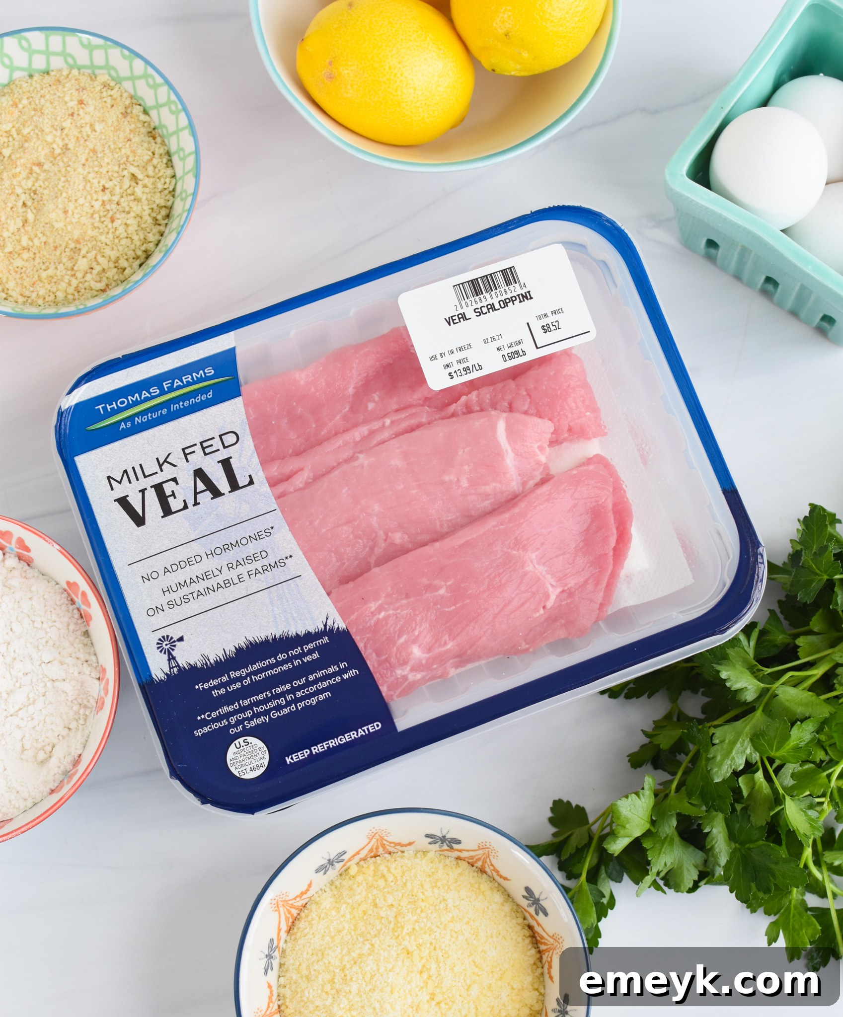 A selection of fresh ingredients including veal scaloppine, eggs, flour, breadcrumbs, Parmesan, and herbs laid out for an easy Veal Milanese recipe.
