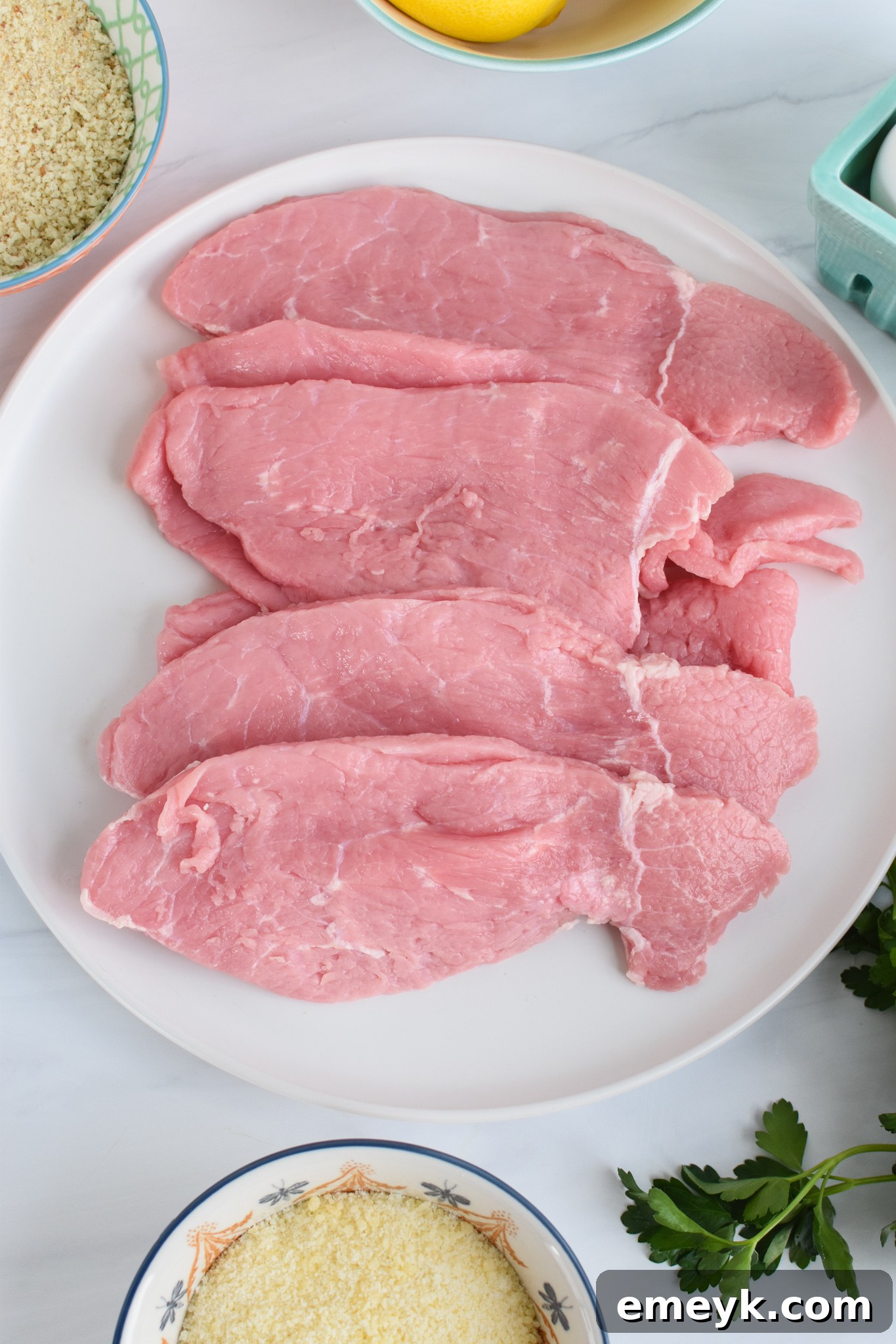 Veal scaloppine being prepared on a plate before breading for Veal Milanese.