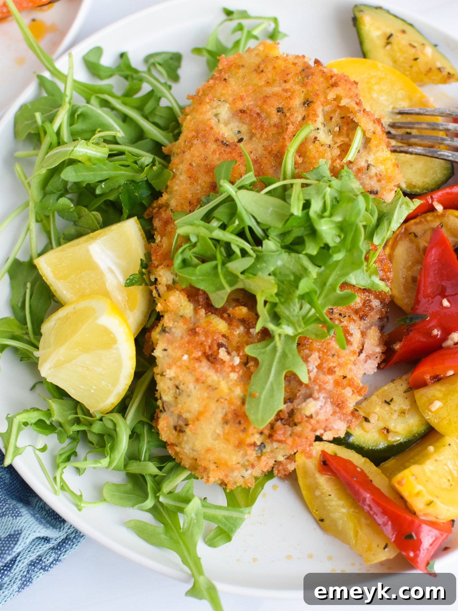 Two pieces of golden-brown Veal Milanese garnished with lemon wedges and fresh arugula, highlighting a vibrant presentation.