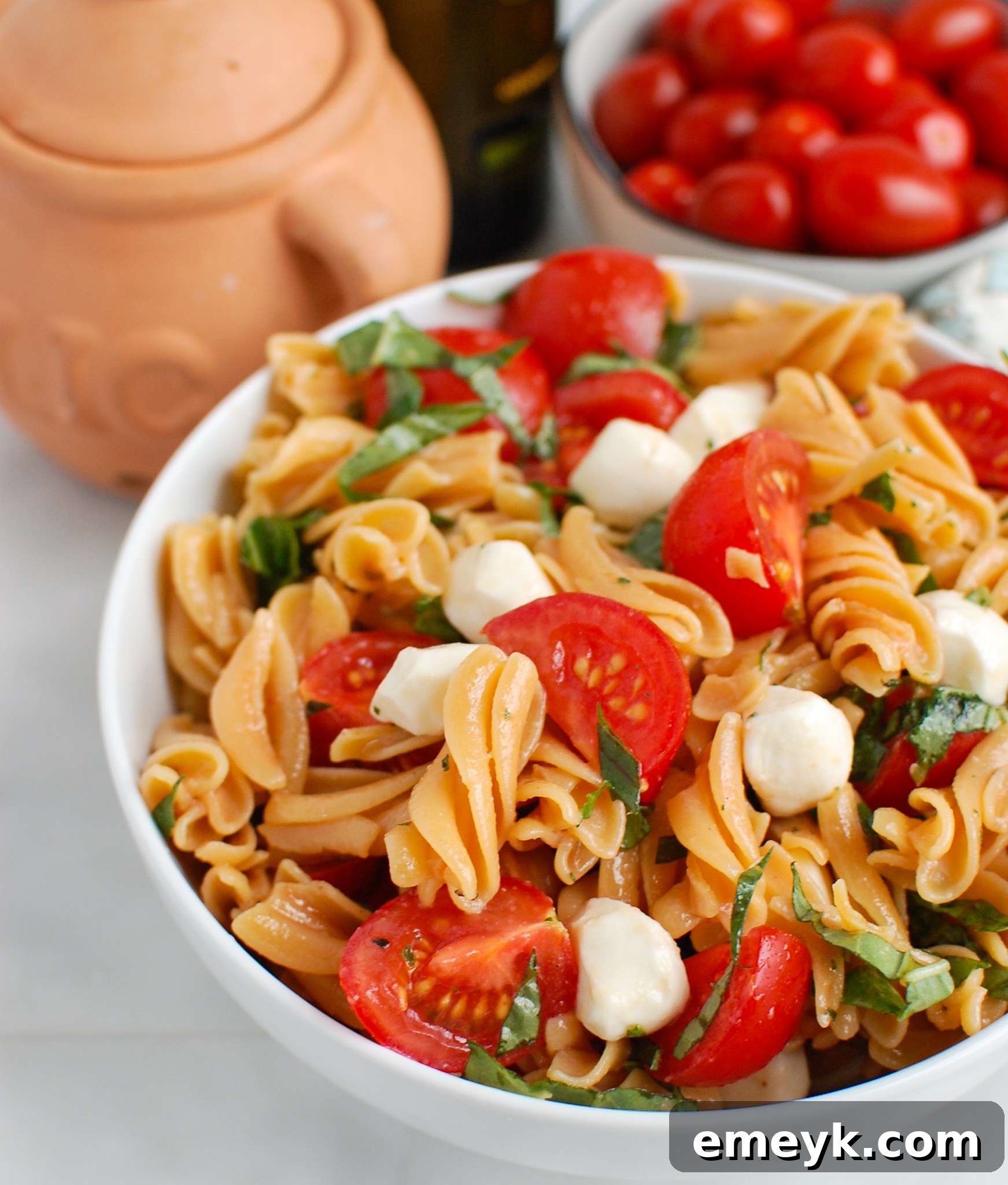 Caprese Pasta in white bowl, garnished with fresh basil
