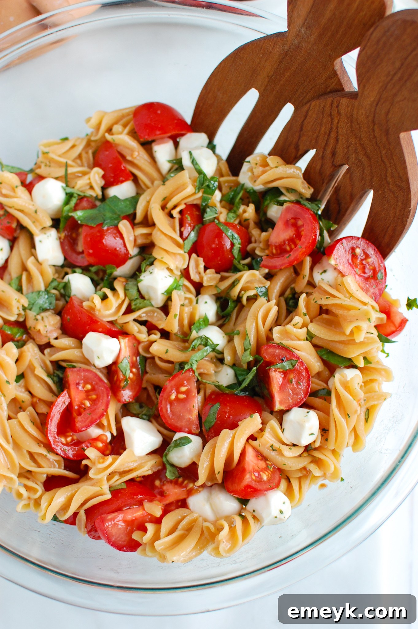Caprese Pasta being served with wooden tongs