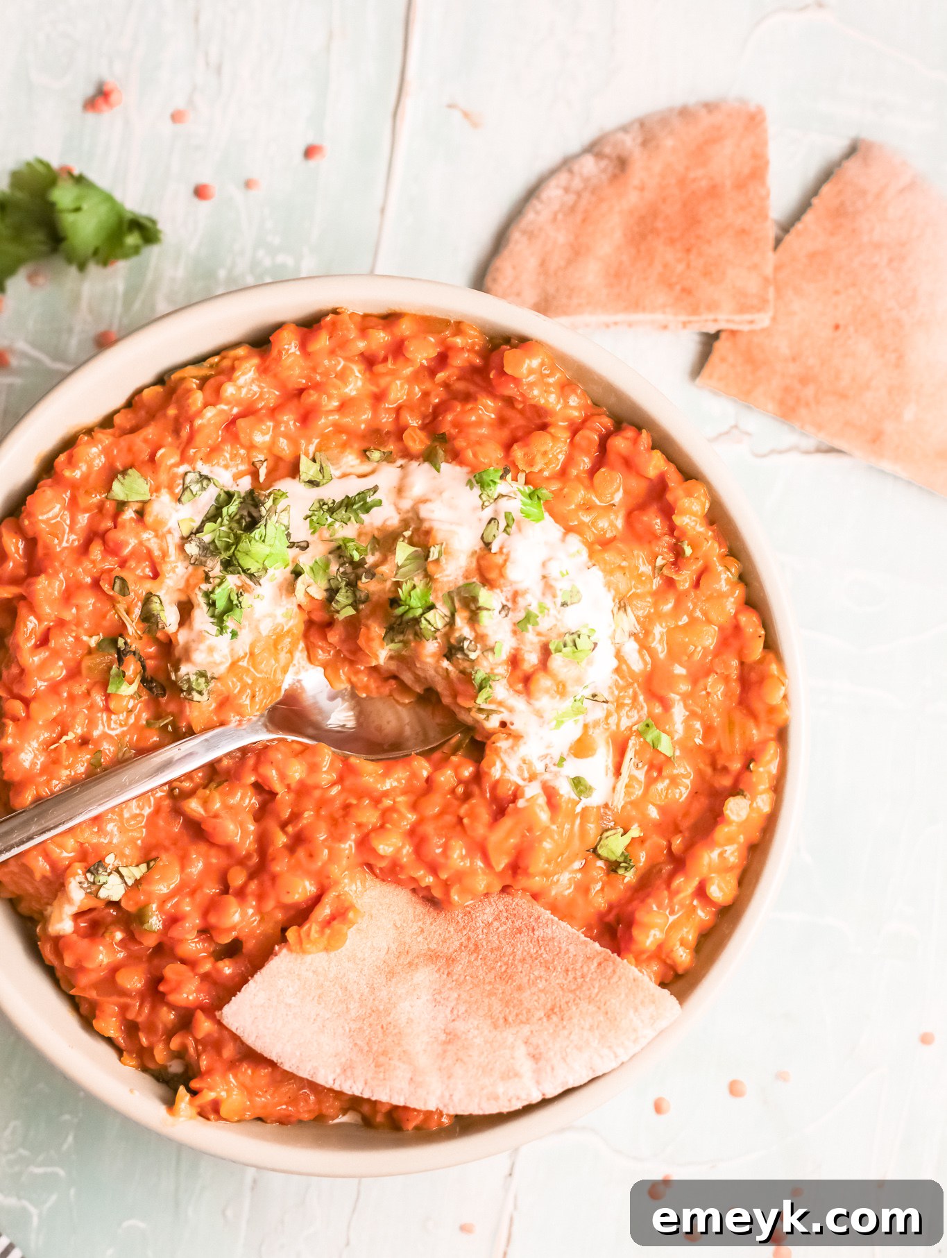 A vibrant bowl of Red Lentil Curry topped with fresh parsley, with a spoon resting in it.