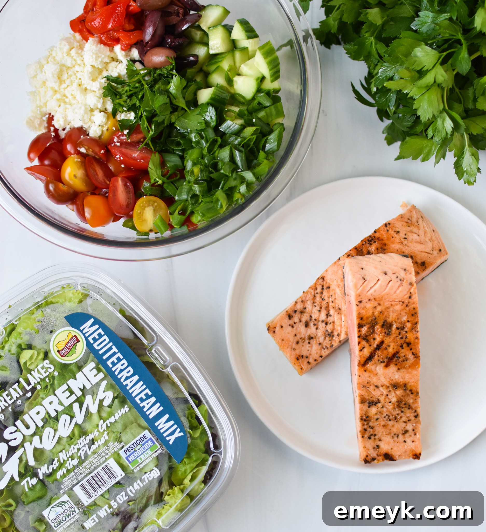 Sun-Drenched Mediterranean Salmon Bowl 3 Ingredients laid out for Mediterranean Salmon Bowl, including salmon fillets, fresh herbs, lemons, olives, feta cheese, and various chopped vegetables.