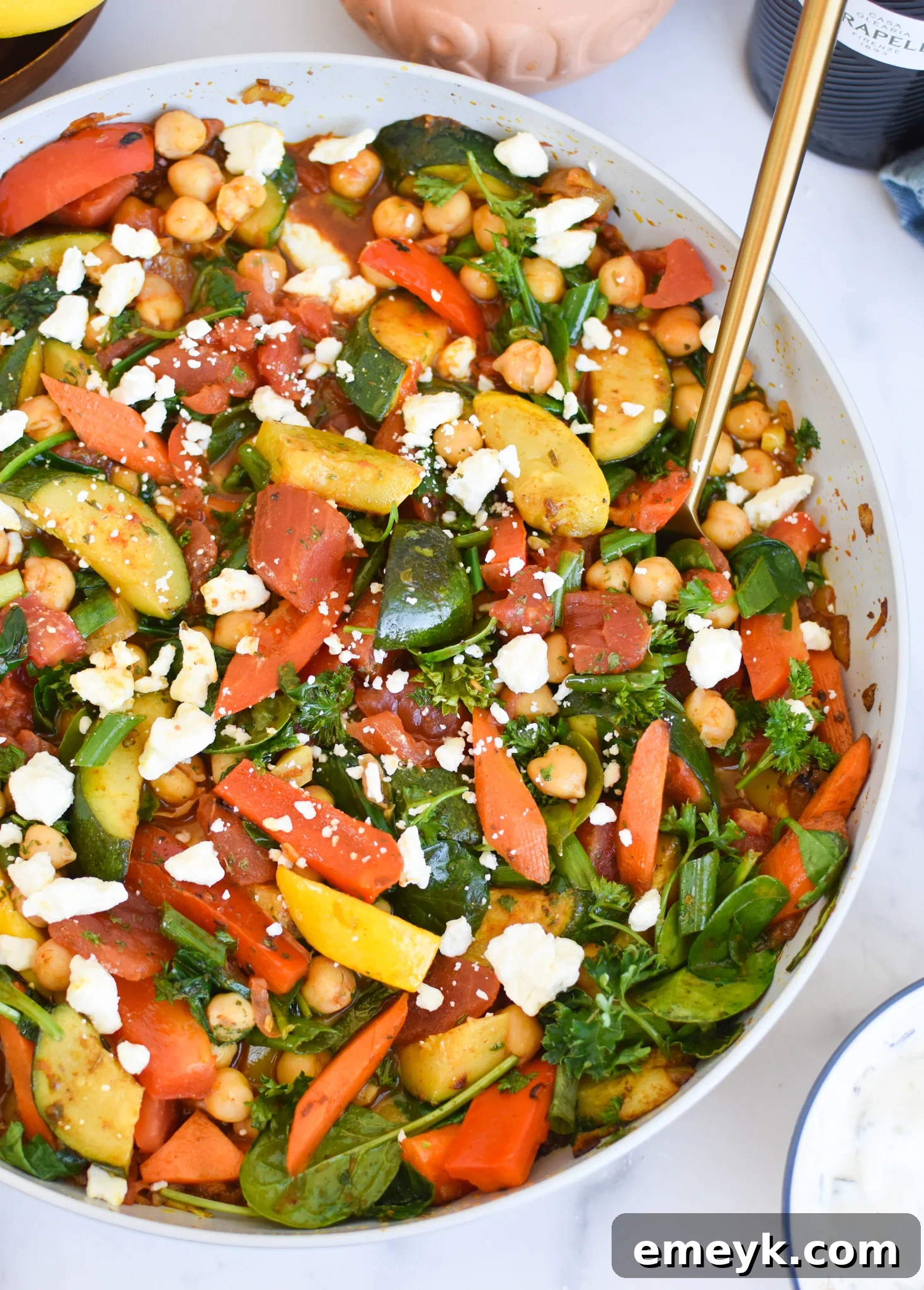 Vibrant Mediterranean Chickpea Skillet 3 Close-up of Mediterranean Chickpea Skillet in a pan, with a gold spoon taking a portion.
