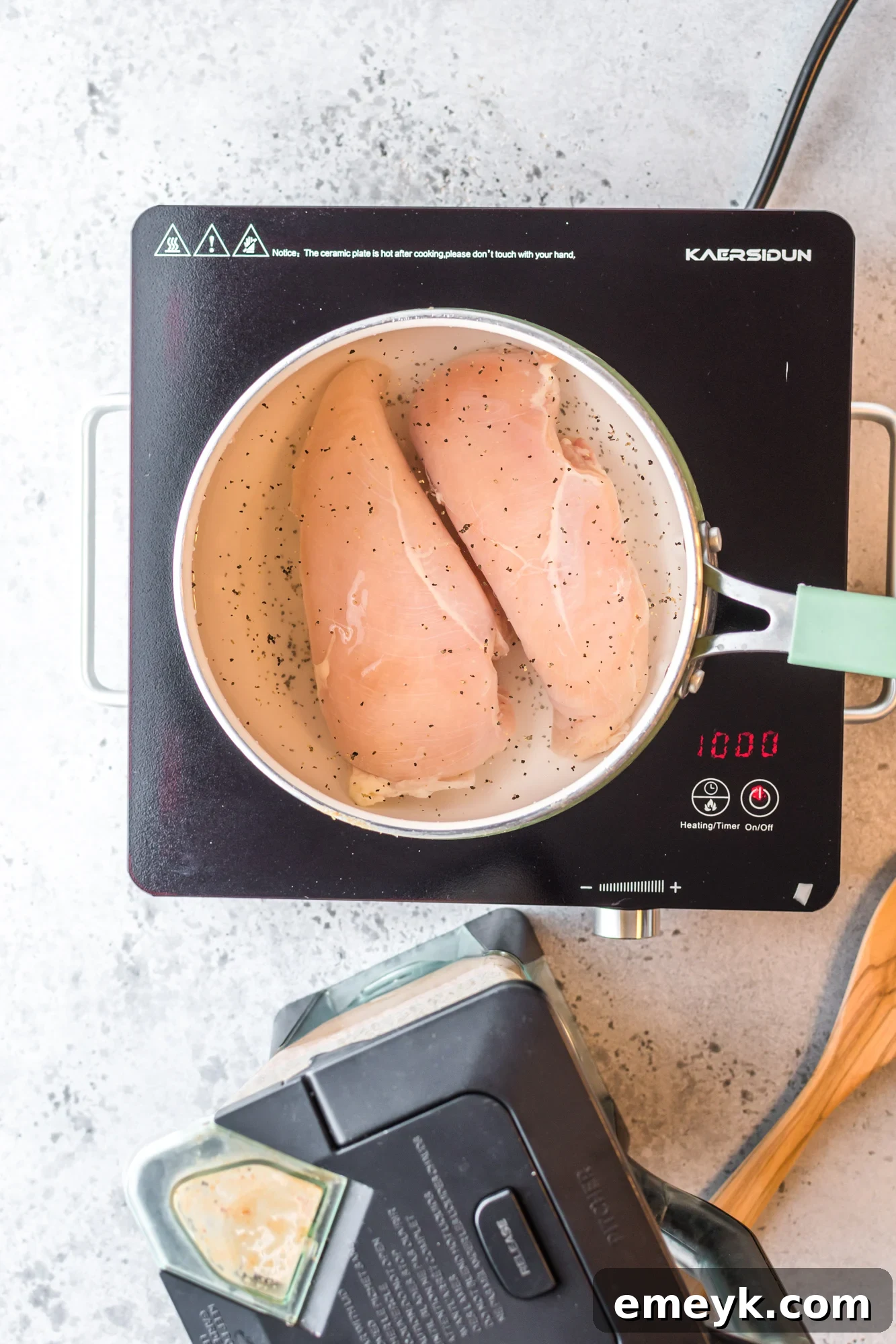 Raw chicken breasts submerged in water in a saucepan, ready to be poached for shredding.