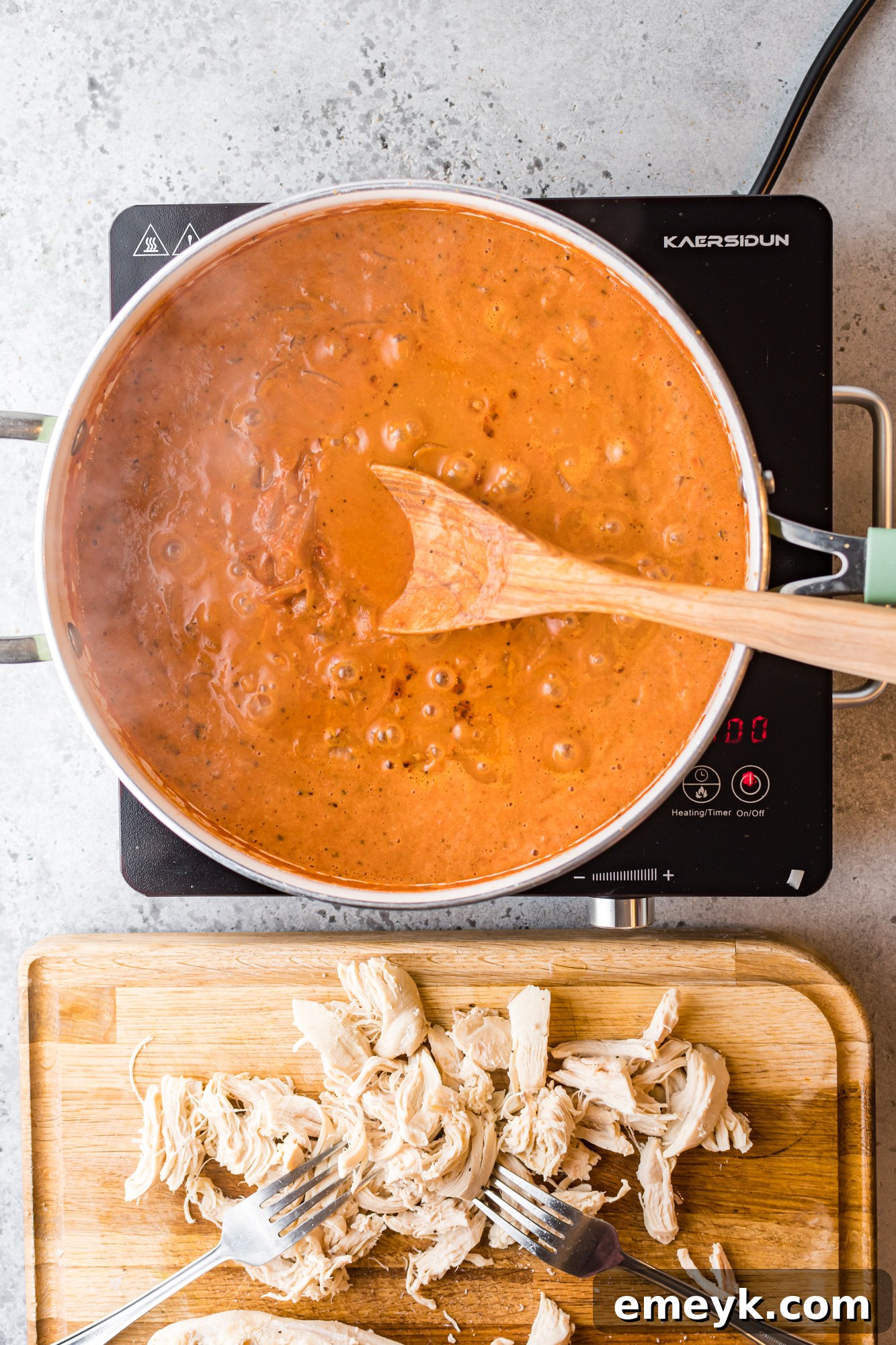 A large spoon scooping into a vibrant pot of Chicken Tinga sauce, showcasing its rich texture and color.