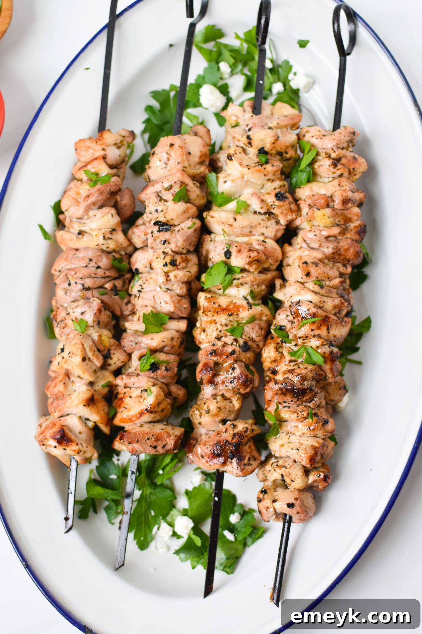 Chicken Souvlaki Recipe on a white platter, garnished with fresh herbs and lemon wedges.