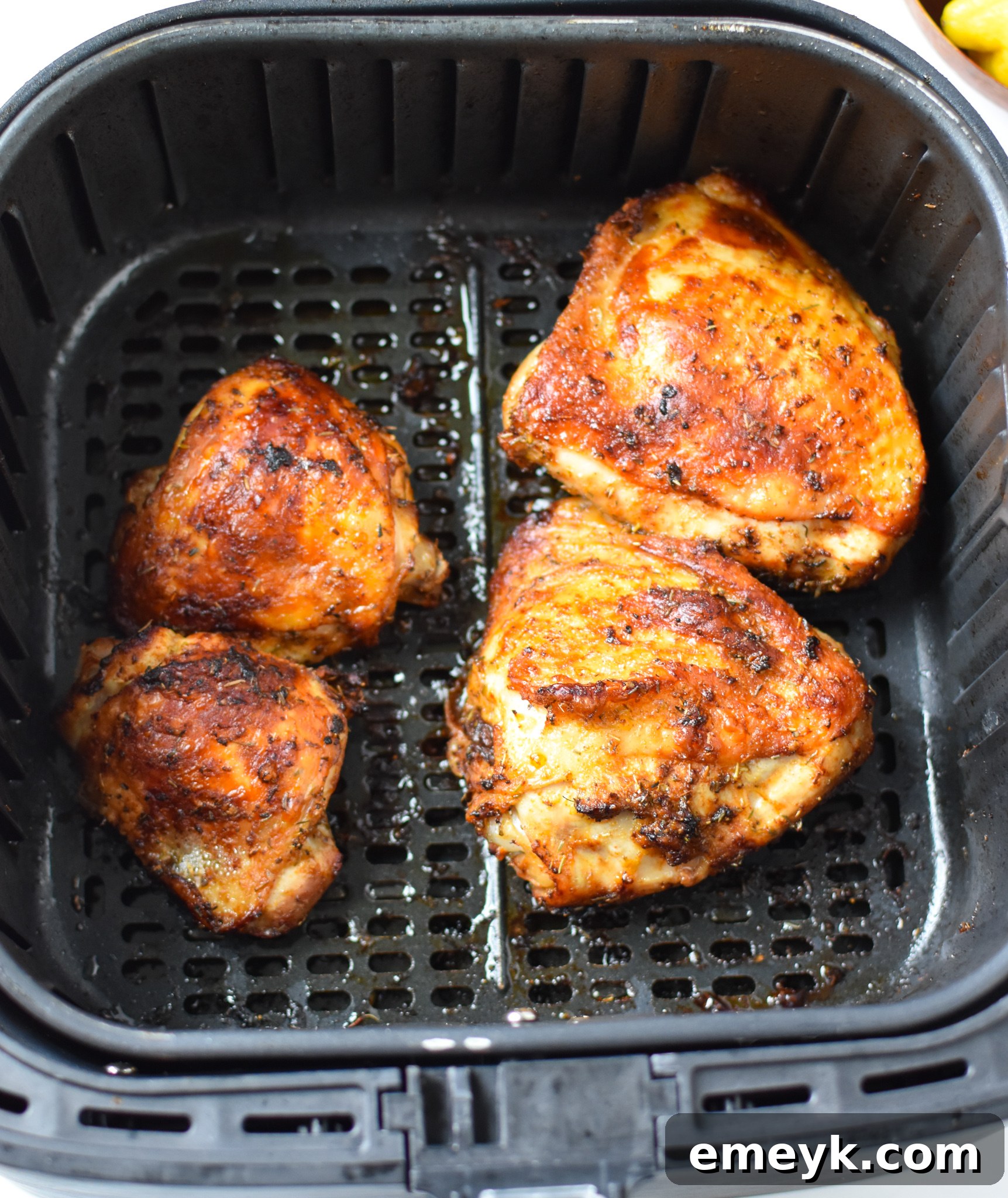Air Fryer Mediterranean Chicken Thighs cooking in an air fryer basket, skin side up.
