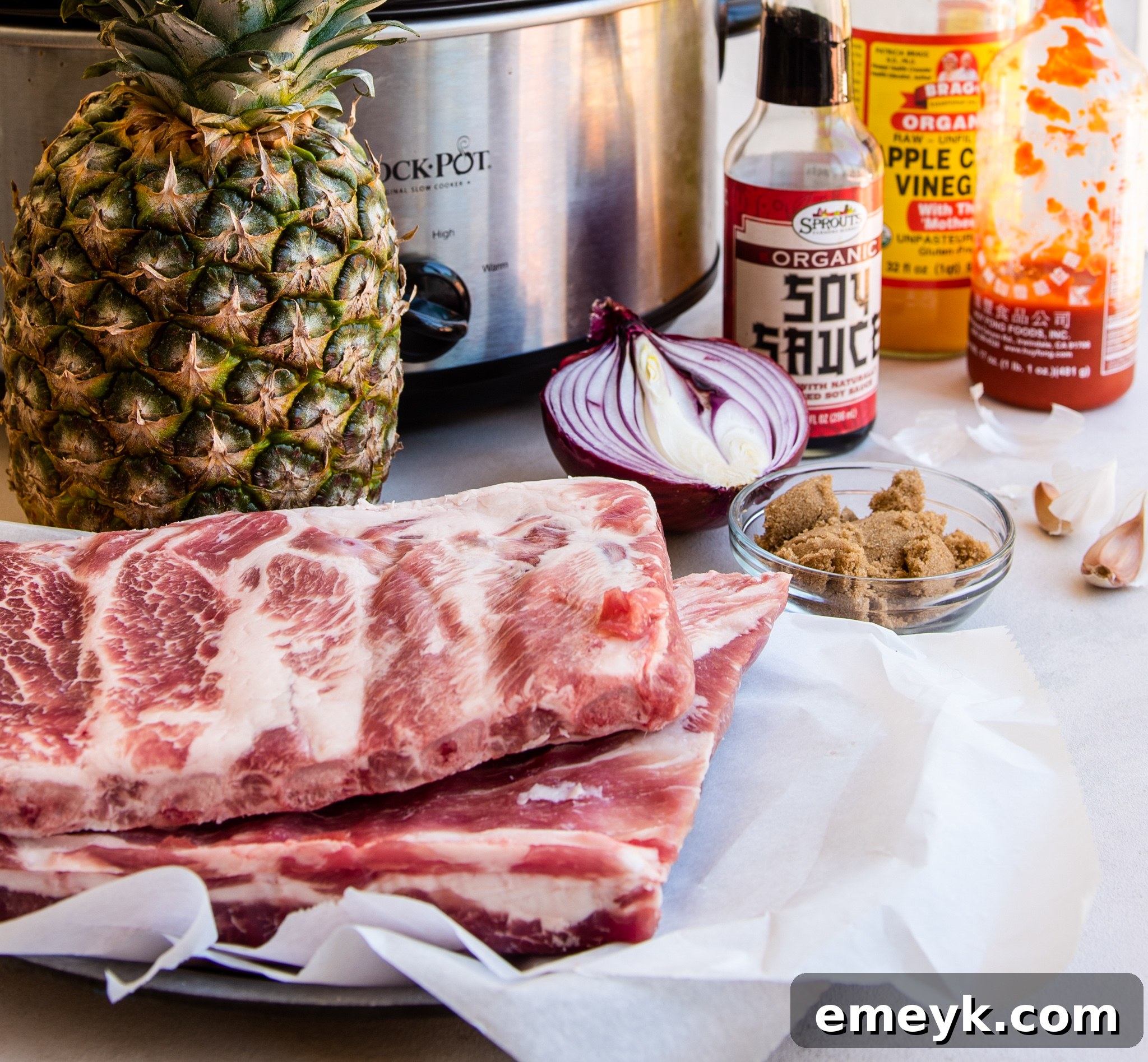 A selection of fresh ingredients including ginger, garlic, pineapple, and sauces, laid out for Slow Cooker Hawaiian Pork Ribs.