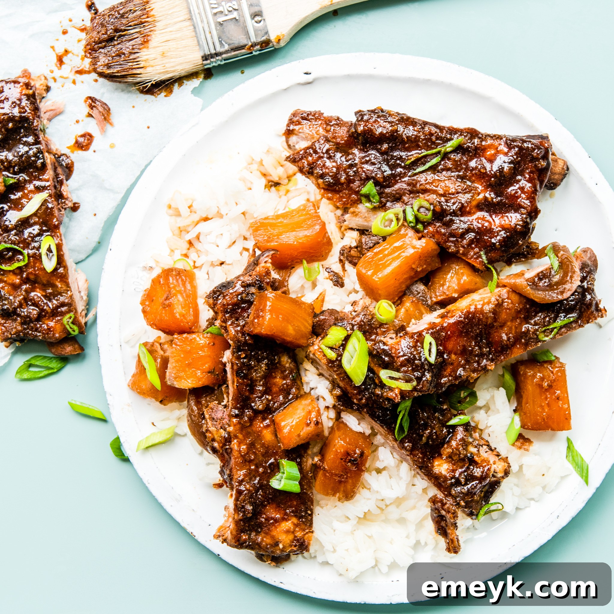 Close-up of a plate of Slow Cooker Hawaiian Pork Ribs with fresh pineapple and green onion garnish.